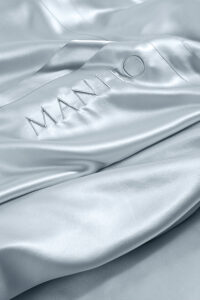 Luxurious MANITO 22 silk flat sheet with signature embroidery in a shimmering close-up, showcasing the elegant finish and craftsmanship.