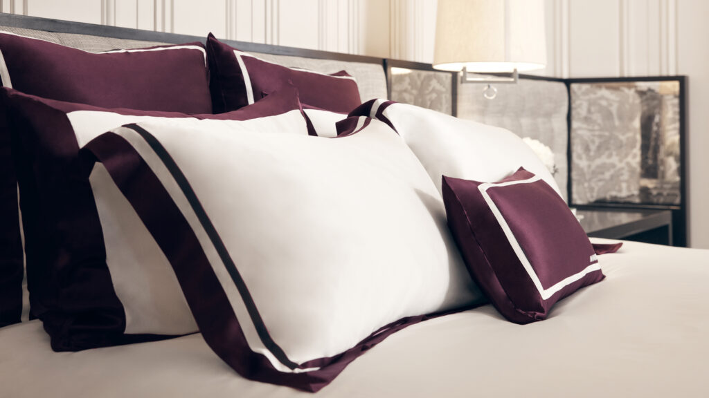 An elegantly made bed with a luxurious set of white and deep burgundy 22 momme silk pillowcases with contrasting borders.