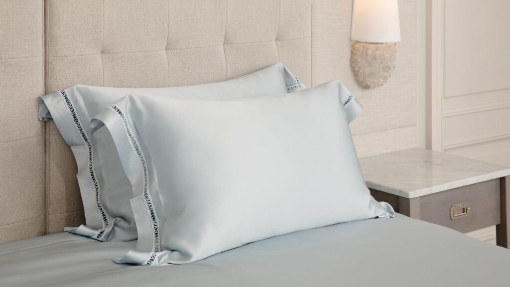 Close-up of a silk pillowcase with embroidered brand name on a luxurious bed setting.