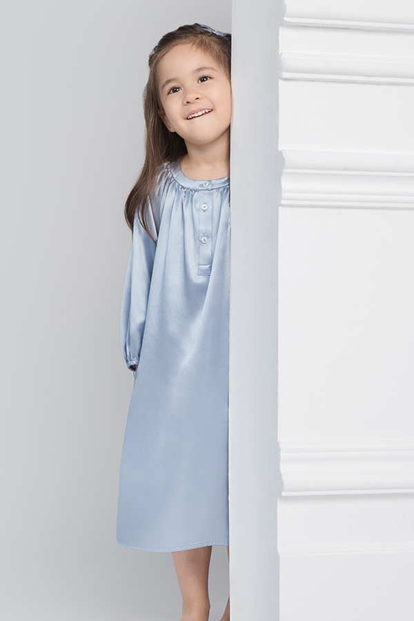 Happy young girl peeking around the wall wearing crystal blue silk nightgown.