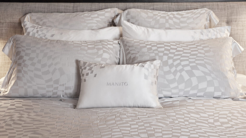 A close-up of a MANITO decorative pillow on a bed made with 22 momme silk sheets featuring an elegant grey checkerboard pattern.