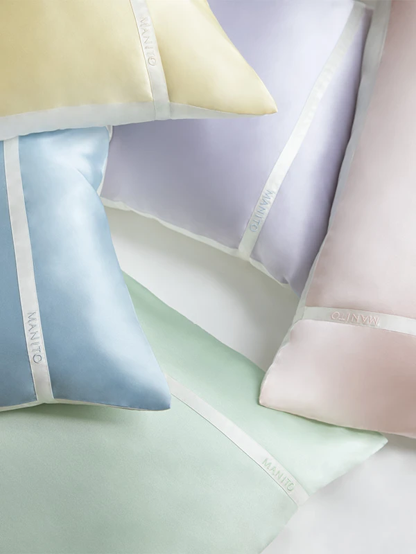 A collection of MANITO pastel silk pillowcases with signature ribbon detail in soft yellow, lavender, mint, blush, and blue tones.