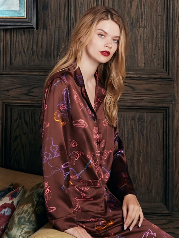 Model wearing MANITO chocolate silk pajama set with playful neon line art prints in a vintage interior.