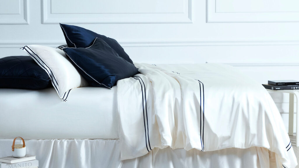 MANITO branded ivory silk sheets with navy accents perfectly laid out on a bed, showcasing premium quality.