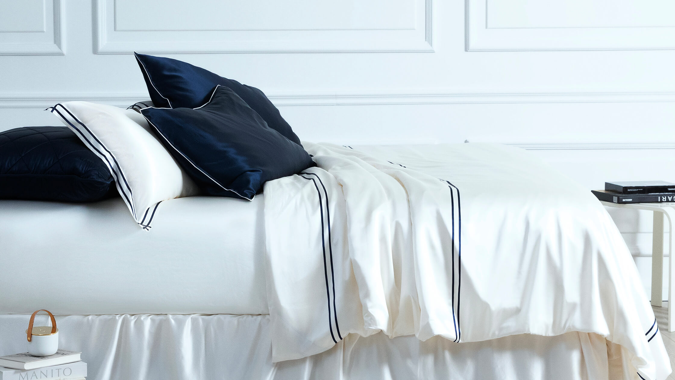 MANITO branded ivory silk sheets with navy accents perfectly laid out on a bed, showcasing premium quality.