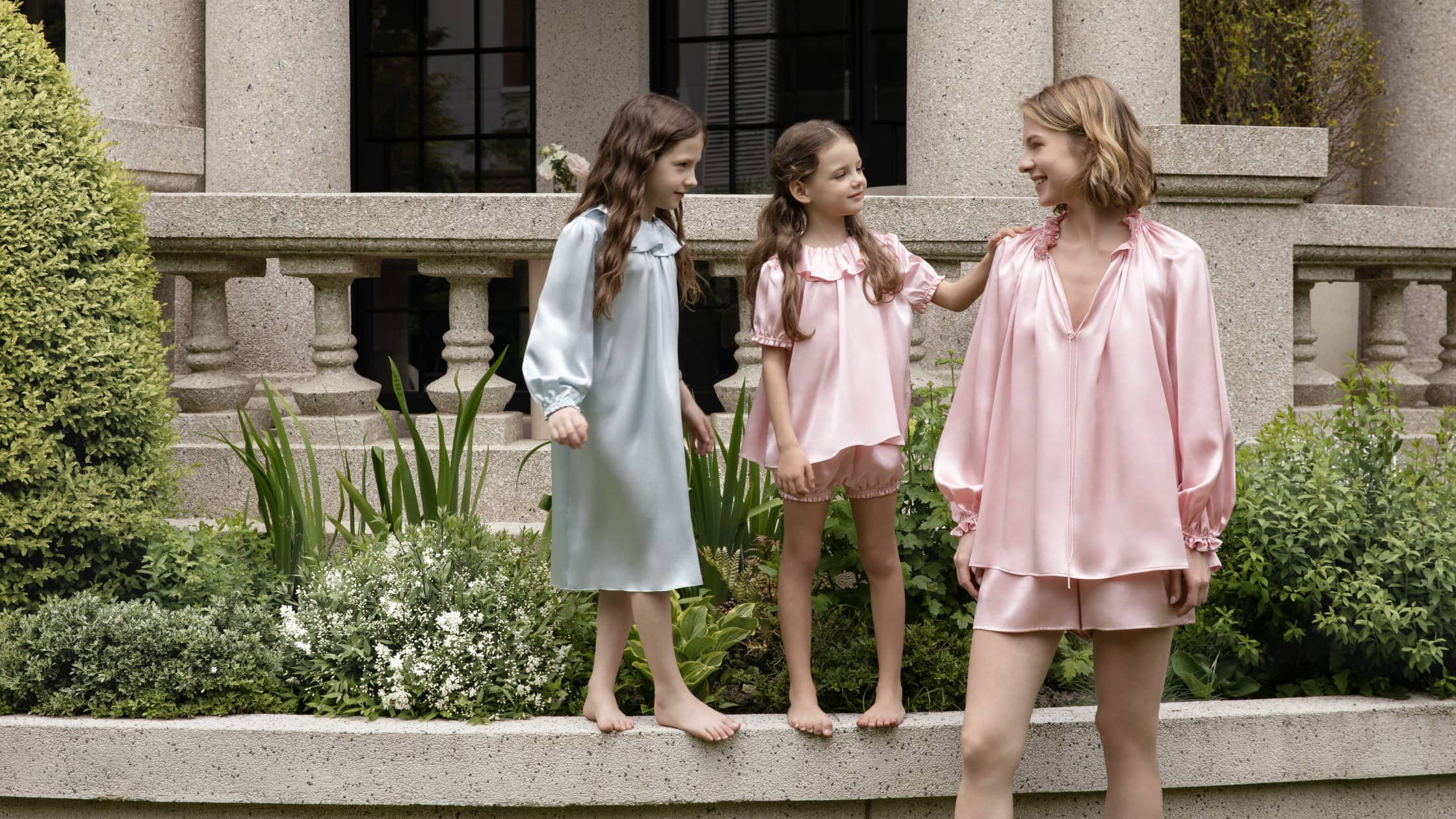 Mother and daughters wearing matching MANITO silk pajamas, enjoying a slow and comfortable family moment outdoors.