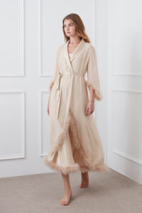 Woman in Diva Feather Trimmed Long Robe in silk georgette with feather trim, standing in a bright indoor space.