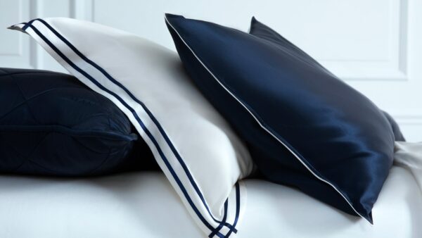 Navy blue and white silk pillowcases with trim detailing on a bed