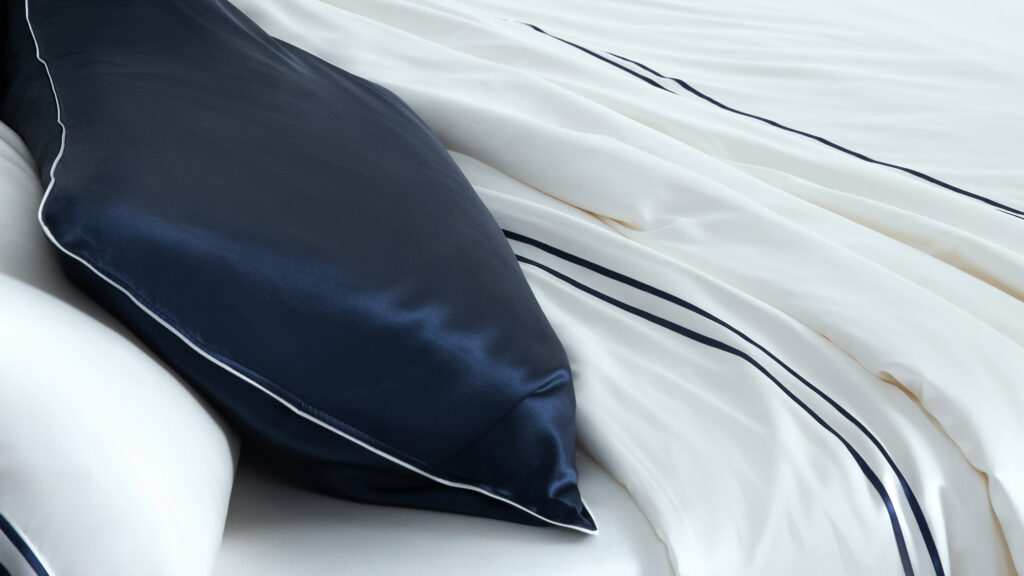 Navy blue silk pillowcase contrasting with ivory silk sheets, highlighting sophisticated bedroom decor.