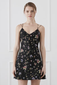 Woman among flowers wearing Lrisette Bow Midi Slip Dress in white floral print with prominent bow detail.