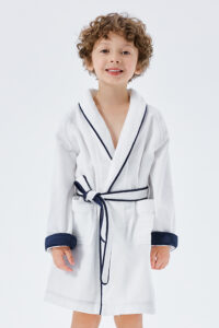 Cheerful curly-haired child in a white silk terry robe with navy trim and tie.