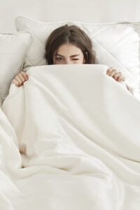 Elegant woman peeking out from a silk-filled duvet, showcasing comfort and luxury.