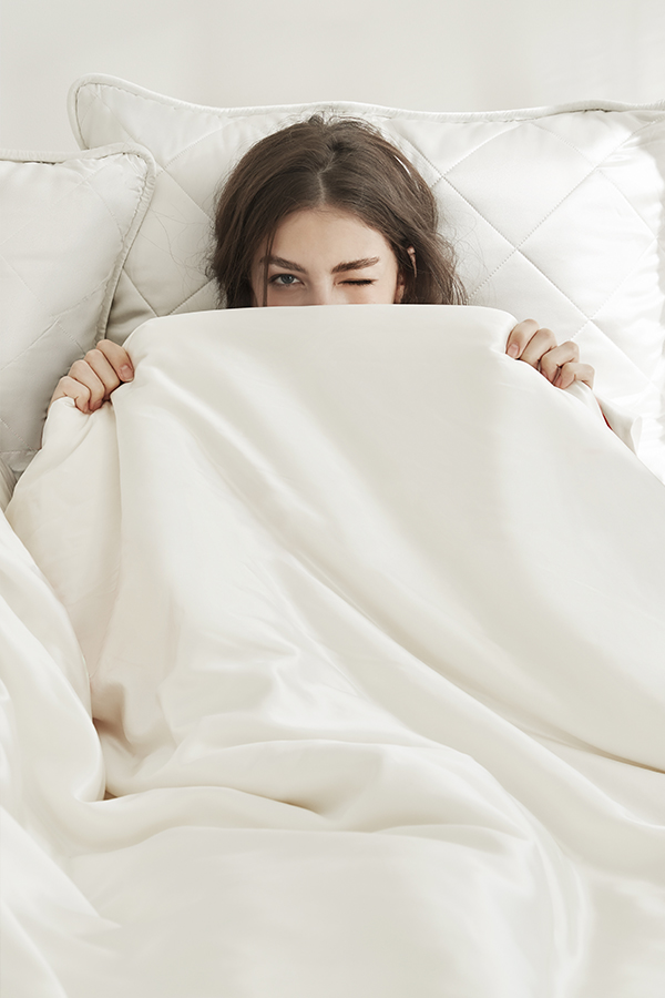 Elegant woman peeking out from a silk-filled duvet, showcasing comfort and luxury.