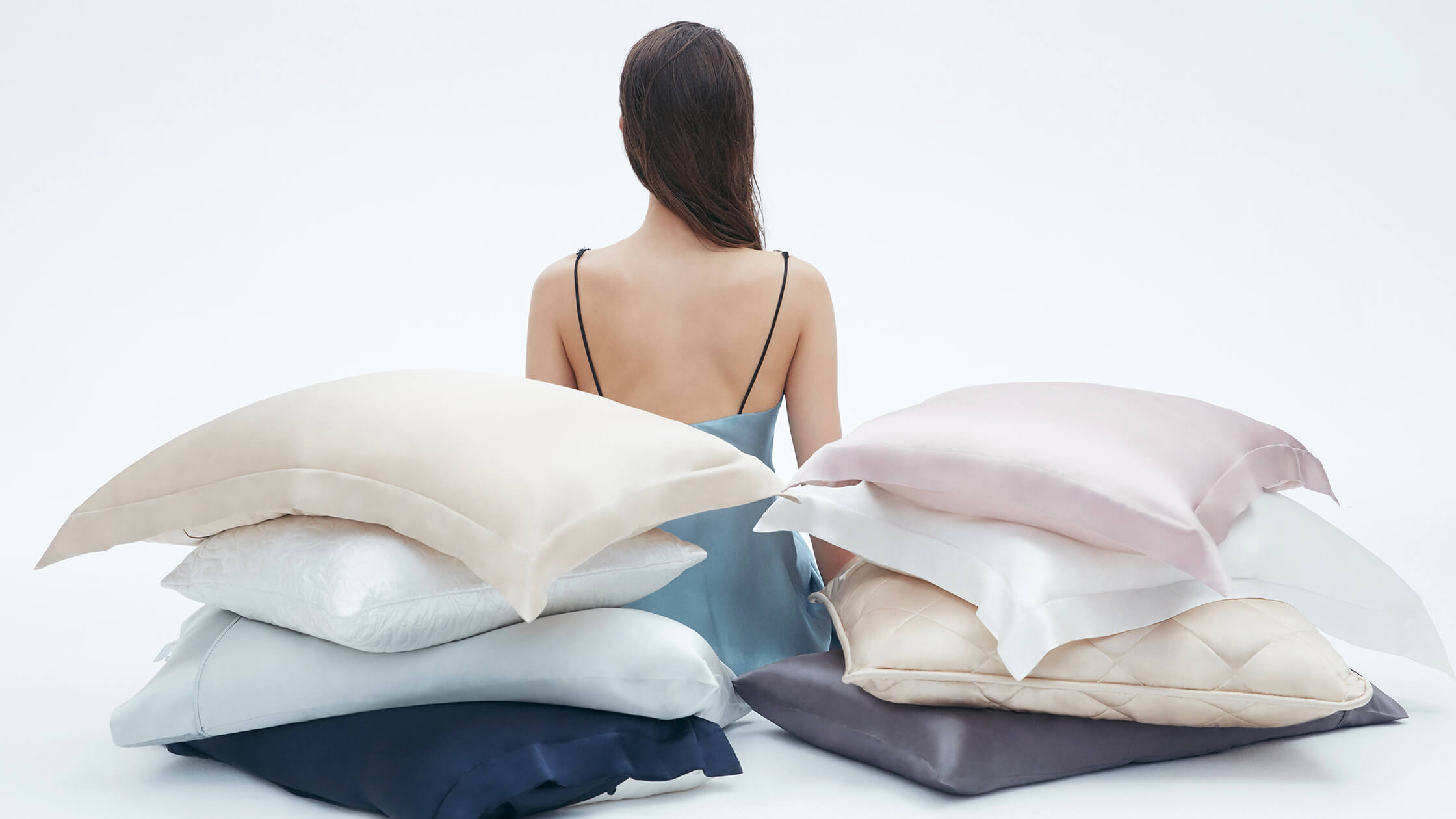 woman sitting amidst a collection of premium pillows, reflecting a moment of relaxation on National Self-Care Day.