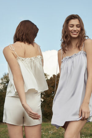 Two women wearing Blooming Camisole & Shorts Set in ivory and lilac silk, enjoying a sunny day outdoors.