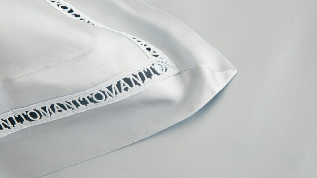 Detailed view of a silk pillowcase corner with intricate embroidery and brand name MANITO.
