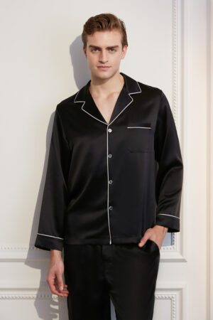 An elegant man in a MANITO Authentic black silk pajama set with white piping details.