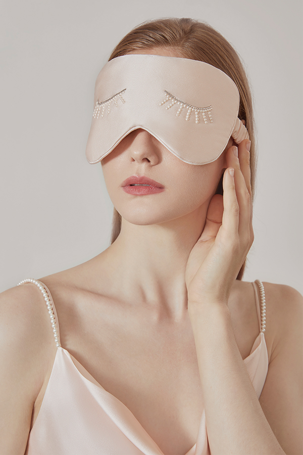 Woman wears Pearlwear Silk Eye Mask in pink, showcasing its pearl-inspired shimmer and elegant sleep comfort.