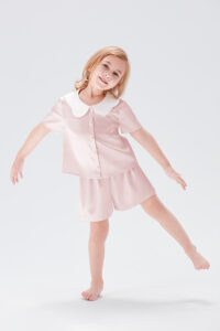Little girl smiling in Doll Kid's Short Pajama Set with peter pan collar in ballet pink.