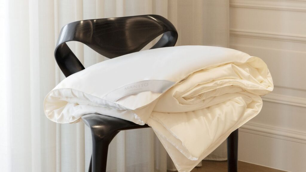 A cream-colored MANITO silk-filled duvet casually draped over a modern black chair.