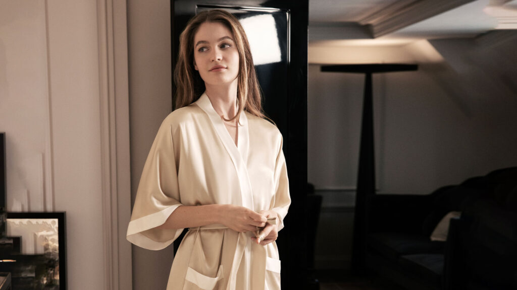 Woman wearing a champagne silk kimono pajama standing in a stylish modern room.