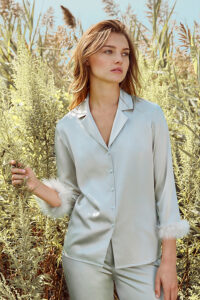 Young woman standing in a Diva Feather Trimmed Silk Pajama Set amidst a lush field.