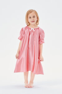Sweet little girl standing in a peach pink Shirley silk nightgown with puffed sleeves.