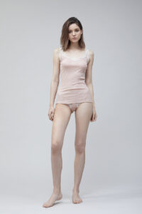 Woman posing in a soft pink Knitting Silk Camisole Top with delicate lace detailing on the edges.